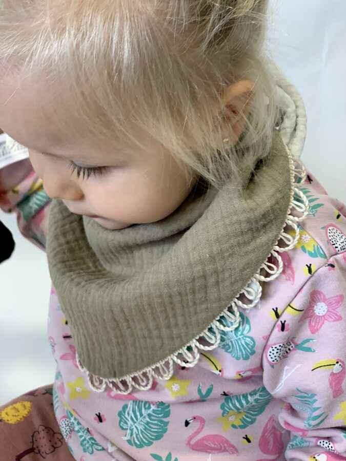 Toddler in a pink patterned outfit wearing a beige muslin bib with lace trim