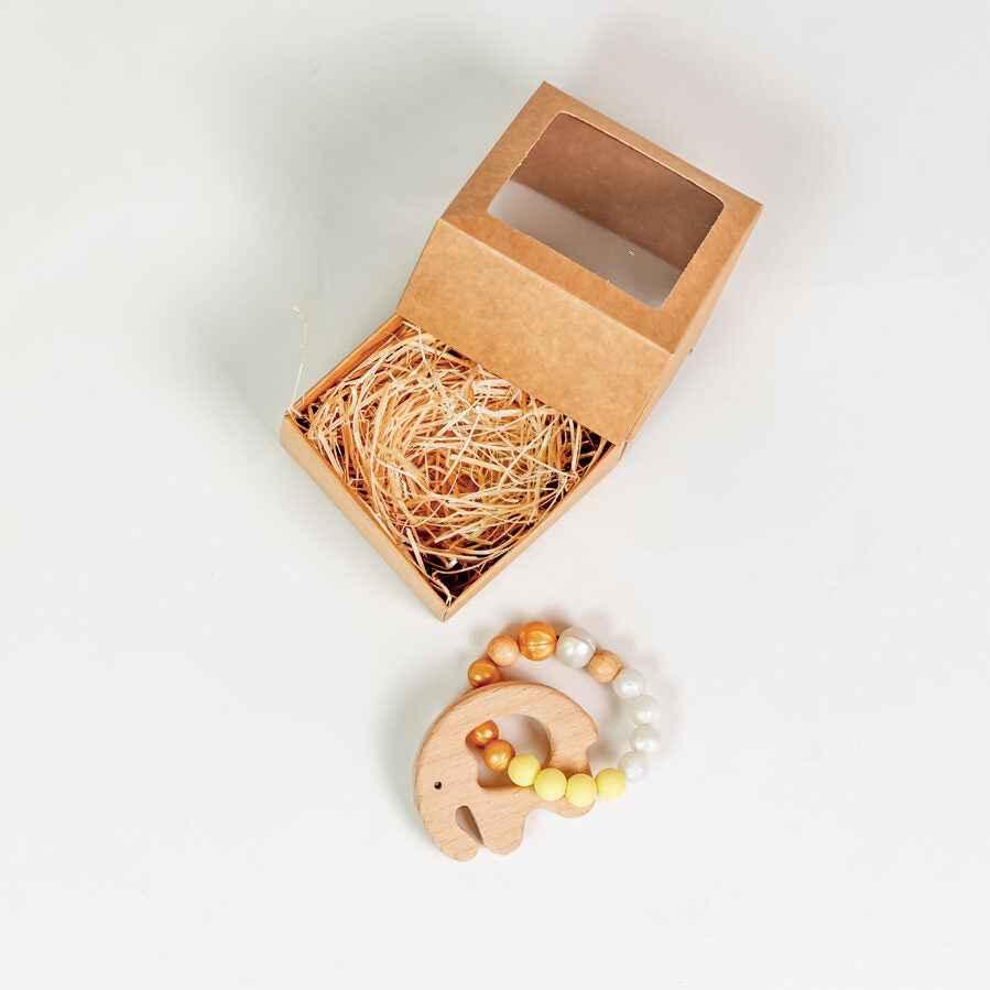 Open kraft gift box with shredded filling and wooden elephant teether with yellow beads
