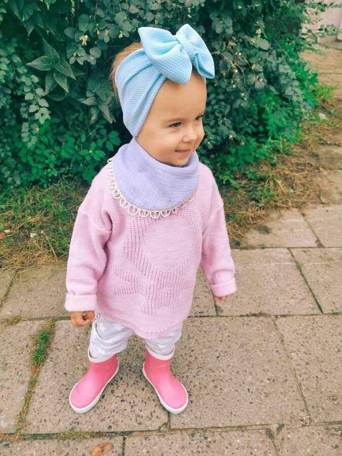 Little girl outdoors in a pale pink teddy-pattern sweater, blue headband, pink boots